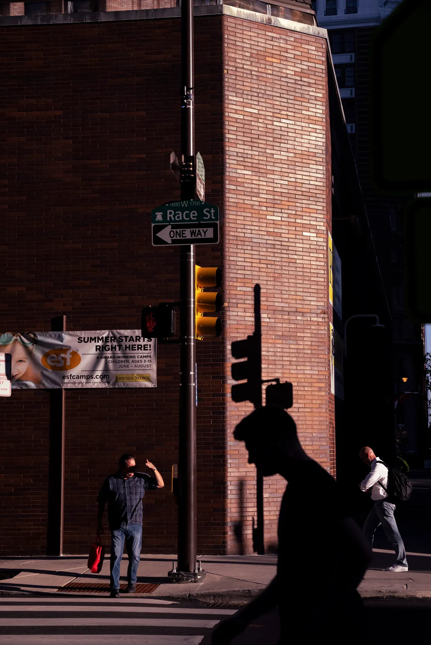 Two silhouettes moving past a sunlit brick wall.