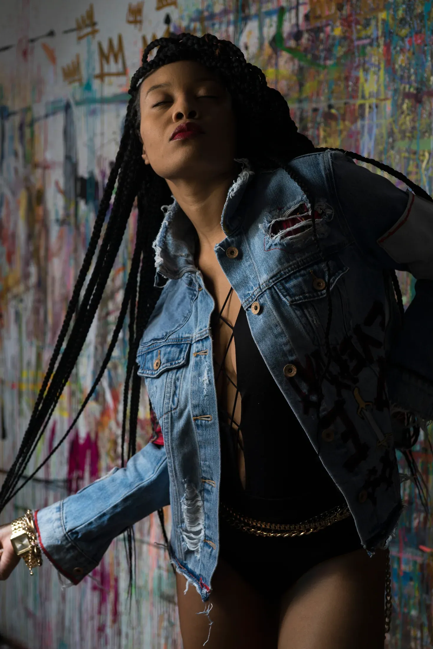 Portrait of a woman in a denim jacket against a painted wall.