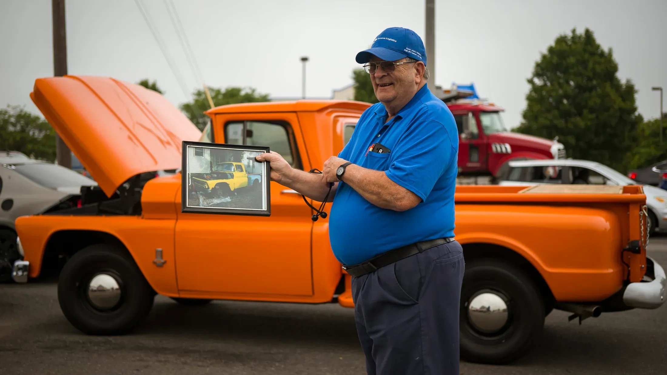 A man standing beside an orange vintage truck.