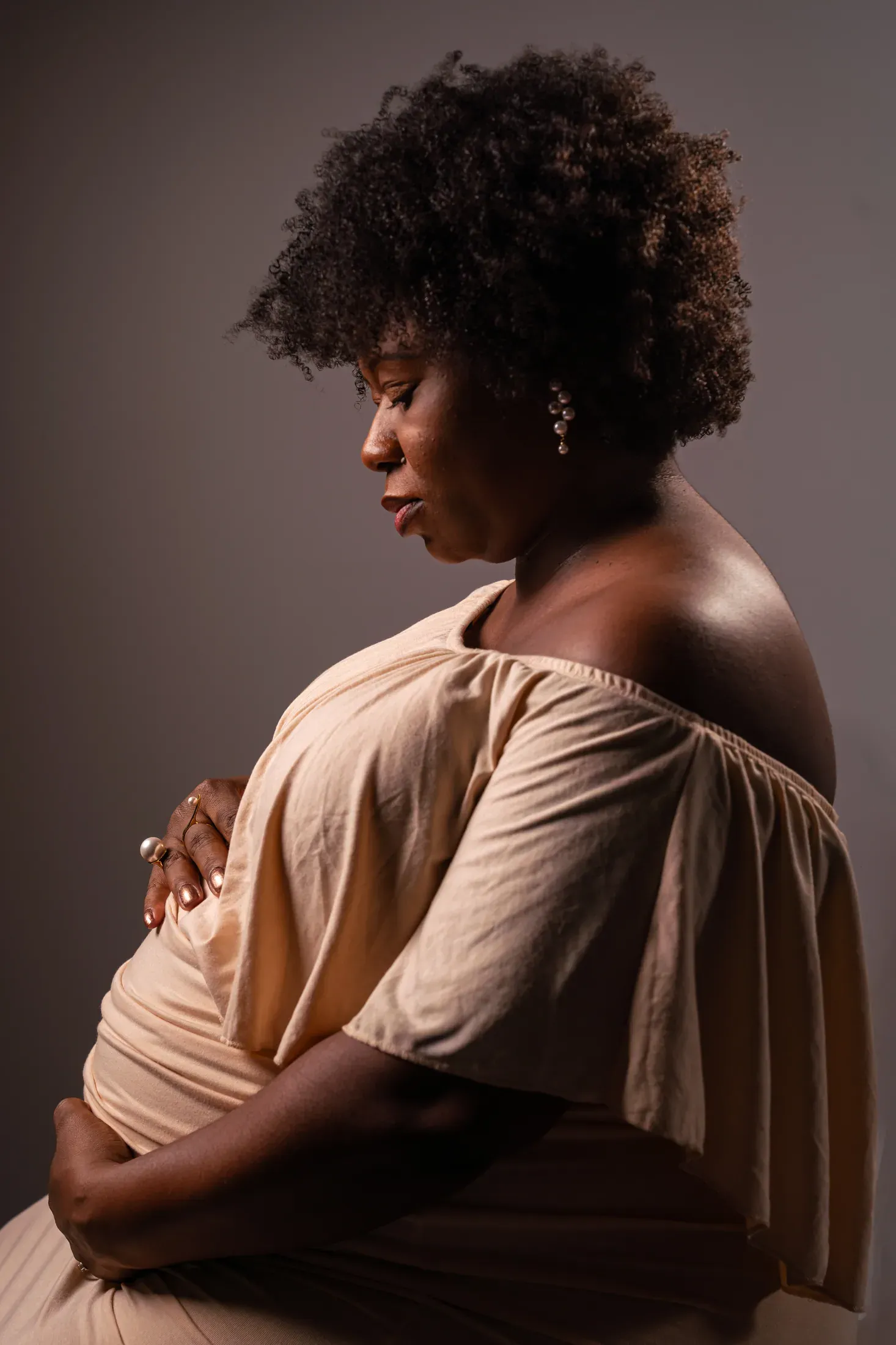 Studio maternity portrait in warm neutral tones.