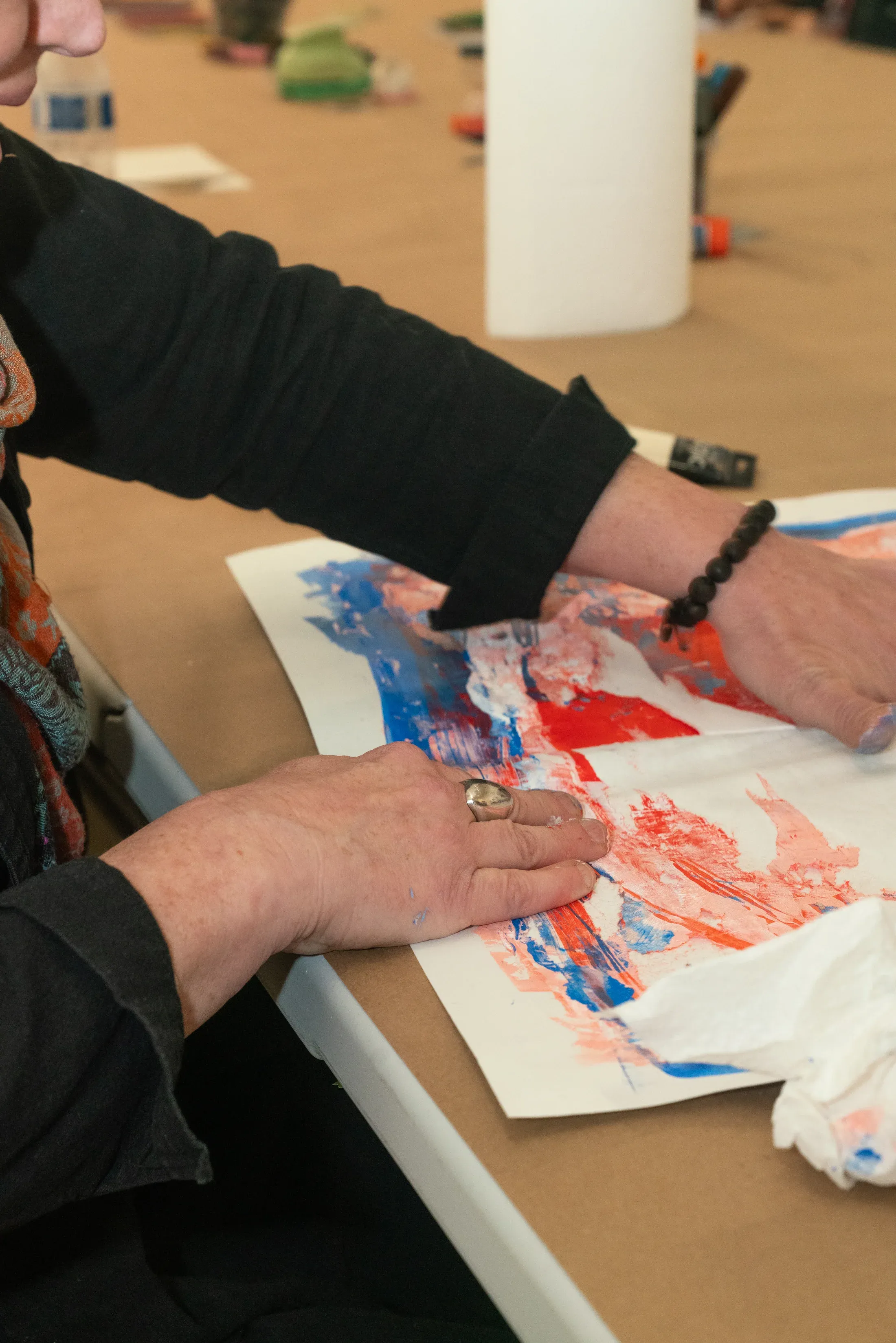 An artist pressing red and blue paint across paper at the shared table.