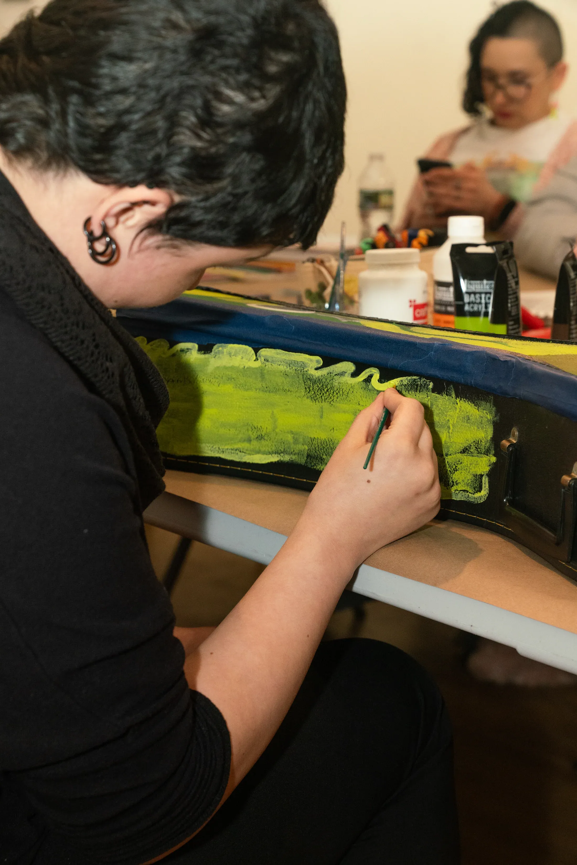 An artist painting a guitar case by hand during an Artist's Table gathering.